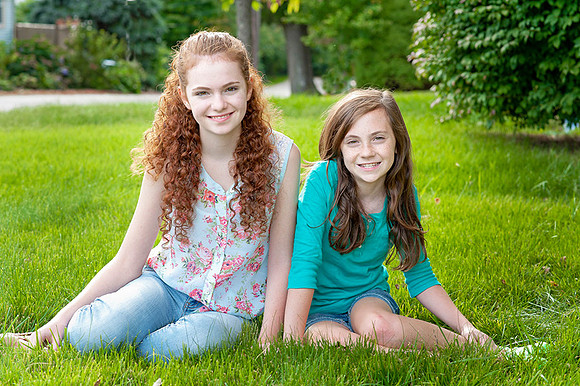 sibling teen sisters sitting on grass in the spring portrait