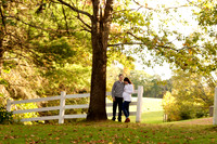 mom and dad maternity session standing under tree near fence at farm