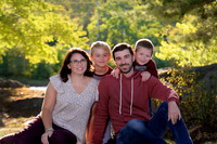 family casually sitting on the grass in the park by a lake during early fall